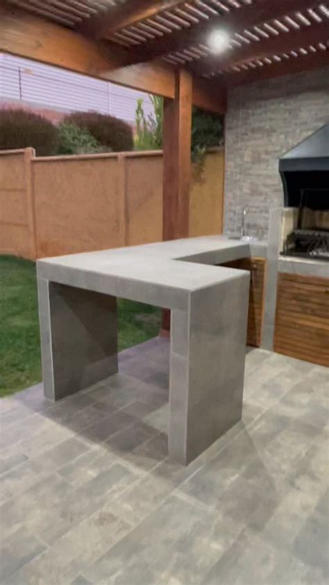 An Outdoor Kitchen With A Grill And Table In The Middle Next To A Back