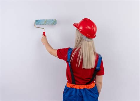 Jeune Fille Blonde Ingénieur Constructeur En Peinture Uniforme Mur Avec Rouleau à Peinture
