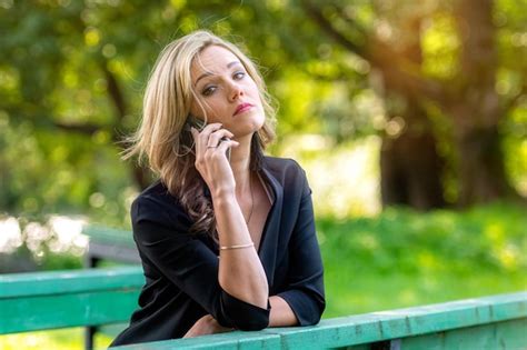 Eine junge emotionale blonde frau sich auf ein brückengleis im park lehnt und am telefon