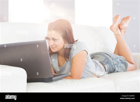 Content Brunette Woman Lying On Her White Couch While Using Her