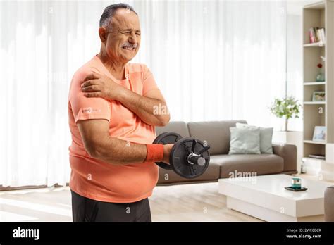 Mature Man Suffering From Painful Shoulder And Exercising With Weights At Home Stock Photo Alamy