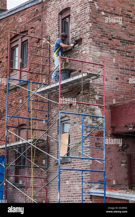 A Brick Mason Works On A Scaffolding Three Stories High To Repair A