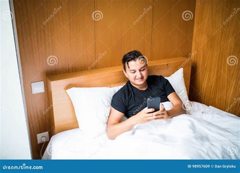 Handsome Young Man In Pajamas Using A Cellphone While Lying In Bed In