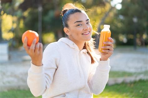 Mujer Morena Bonita Joven Que Sostiene Una Naranja Y Un Jugo De Naranja