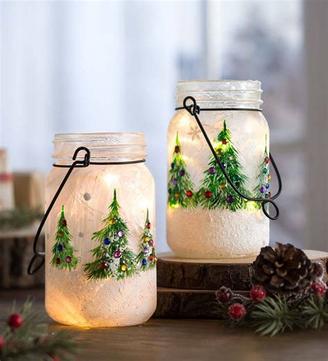 Two Mason Jars Decorated With Christmas Trees And Lights