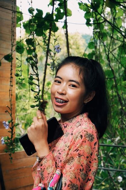 Premium Photo Portrait Of Smiling Woman Standing Against Plants