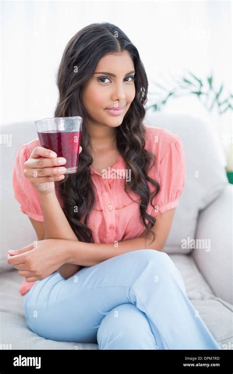 Pleased Cute Brunette Sitting On Couch Holding Glass Of Juice Stock Photo Alamy