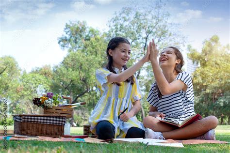 Two Pre Teen Girls Sit On Picnic Mats And High Fiving Each Other At