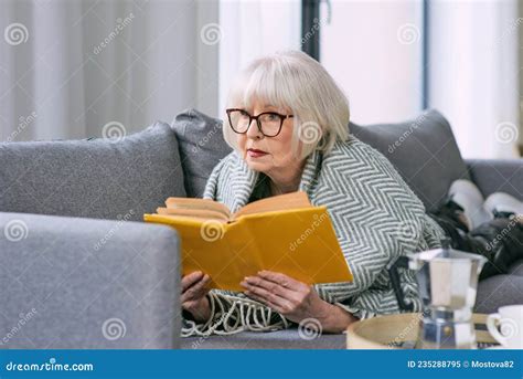 Old Fashioned Senior Woman Laying On The Couch Reading A Book Stock