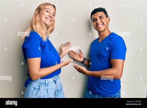 Young Interracial Couple Wearing Casual Clothes Inviting To Enter