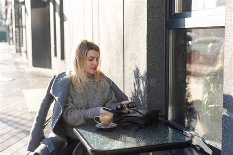 Calm Stylish Mature Woman Sitting At The Cafe Table Outside With Cup Of