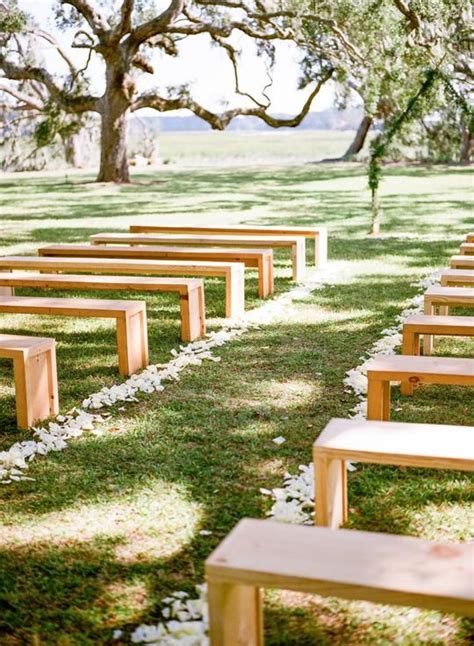 Rows Of Wooden Benches Sitting On Top Of A Lush Green Field Next To A Tree