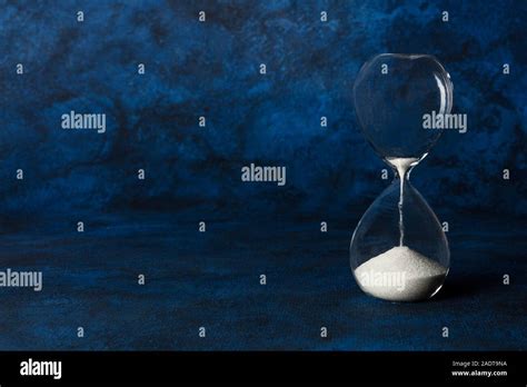 Time Is Running Out Concept An Hourglass With Oozing Sand On A Dark Blue Background With Copy