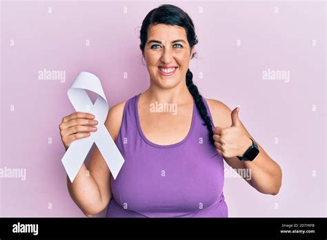 Plus Size Brunette Woman Holding White Ribbon Smiling Happy And Positive Thumb Up Doing