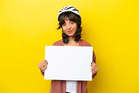 Joven ciclista mujer latina aislada de fondo amarillo sosteniendo un cartel vacío con expresión