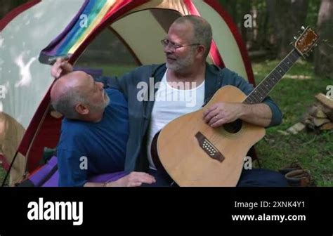 Two Gay Men In Front Of Tent With Pride Flag At Campsite Taking Selfie