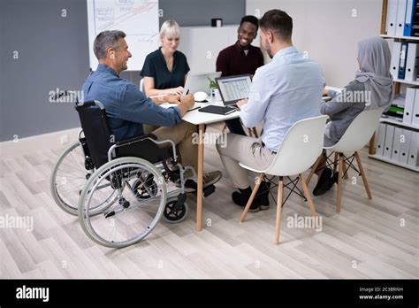 Disabled Mature Businessman Sitting At Desk With Laptop In Conference