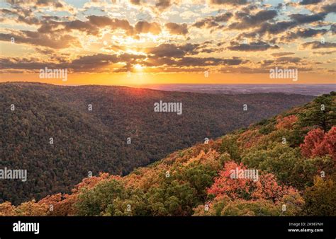 Sun setting behind clouds illuminating the fall colors of the trees in Coopers Rock State Forest ...