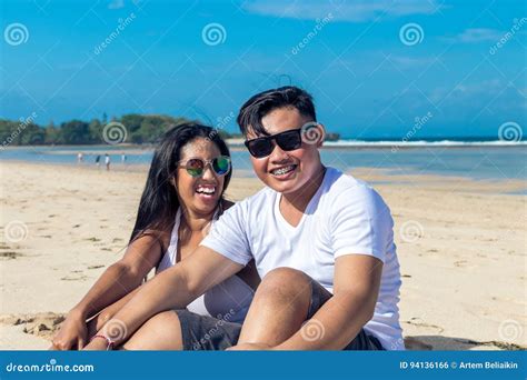 Asian Couple Sitting On The Beach Of Tropical Bali Island Indonesia