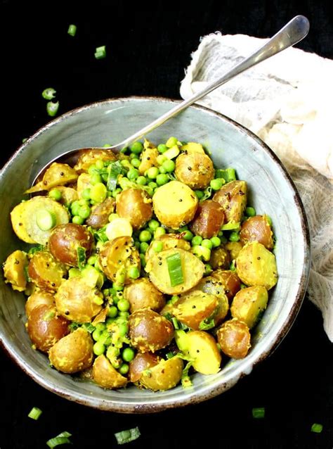 A Bowl Filled With Potatoes And Peas On Top Of A Black Tablecloth Next