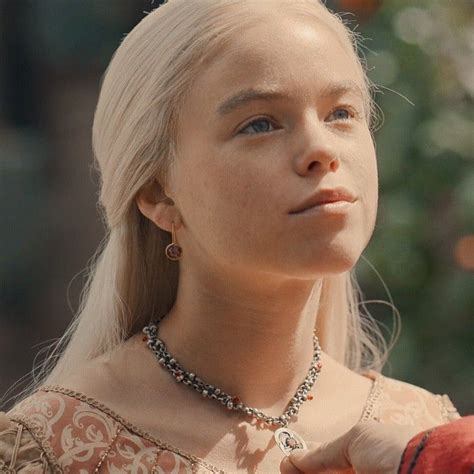 A Woman With Long Blonde Hair Wearing A Necklace And Holding An Apple