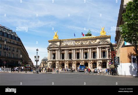 Famous Opera House In Paris People Cross Street And Vehicles Are In