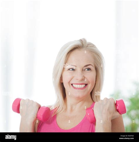 Happy Middle Aged Woman Lifting Dumbbells At Home In Living Room