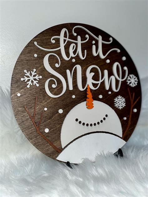 A Wooden Sign That Says Let It Snow On Top Of A White Fur Covered Surface