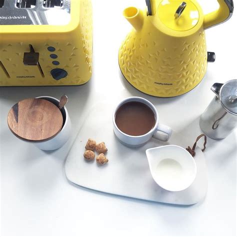 A Yellow Tea Kettle Sitting On Top Of A Counter Next To Cups And Saucers