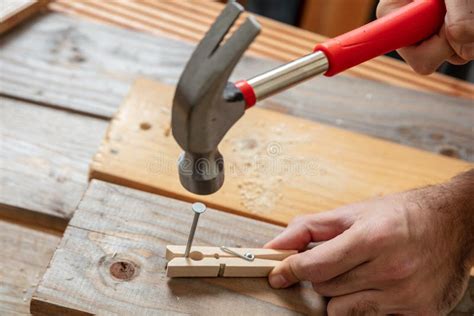 Male Hand Hold Hammer And Nail A Clothespin Wooden Bench Background