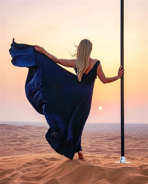 A Woman In A Long Blue Dress Is Standing On The Sand With Her Arms