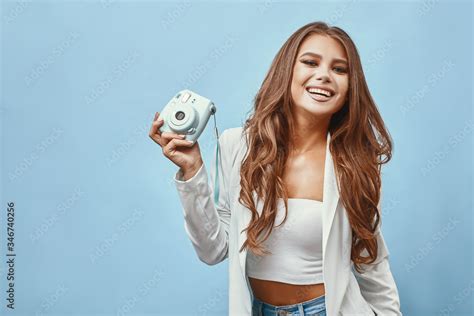 Beautiful Blonde Girl With A Camera In Her Hand In The Studio On A Blue Background Stock Foto