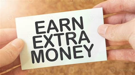 EARN EXTRA MONEY word inscription on white card paper sheet in hands of