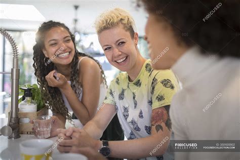 Happy young women friends laughing and talking in kitchen — sitting ...