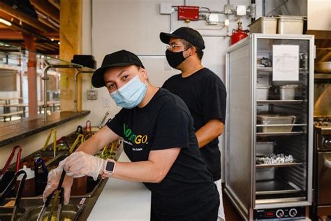 Two People Wearing Masks And Gloves In A Kitchen