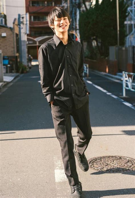 A Man In Black Shirt And Pants Walking Down The Street With His Hands