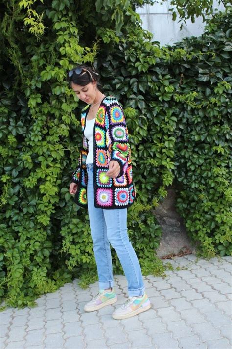 A Woman Standing In Front Of A Green Bush Wearing A Multicolored