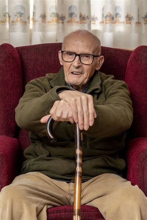 Elder Caucasian Man Holding A Wooden Cane While Sitting On A Red Couch