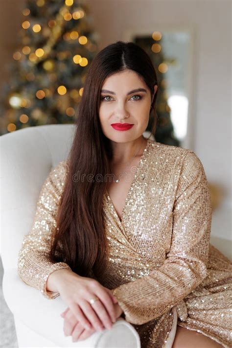 Gorgeous Woman In Golden Dress Sitting On Chair In Christmas Decorated