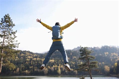 Hombre feliz con los brazos abiertos saltando lago y montañas en el