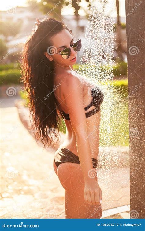 Una Mujer En Un Bikini Que Se Coloca Debajo De Una Ducha Al Aire Libre
