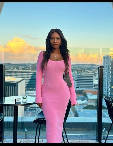 A Woman Standing In Front Of A Window Wearing A Pink Long Sleeved Dress