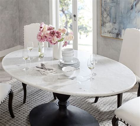 A Dining Table With White Chairs And Flowers In Vases On The Top Next