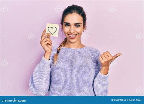 Young Hispanic Girl Holding Heart Reminder Pointing Thumb Up To The