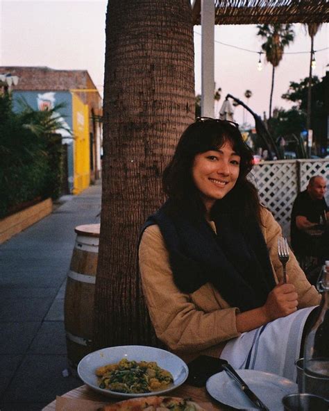 A Woman Sitting At An Outdoor Table With Food And Drinks In Front Of