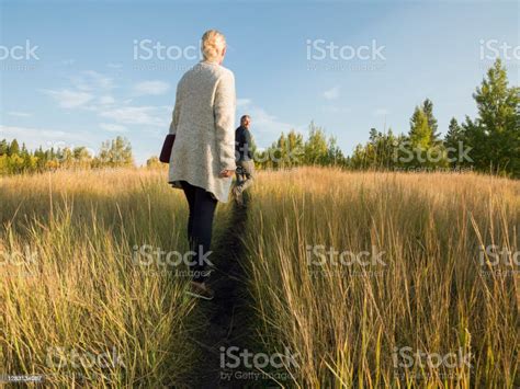 Woman Walks Down Narrow Path Through Tall Grasses Towards Man Stock