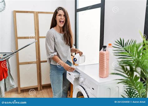 Young Brunette Woman Putting Detergent In Washing Machine Angry And Mad