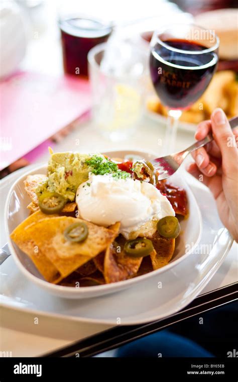 A bowl of nacho chips with salsa, guacamole, jalapenos, cheese and sour ...