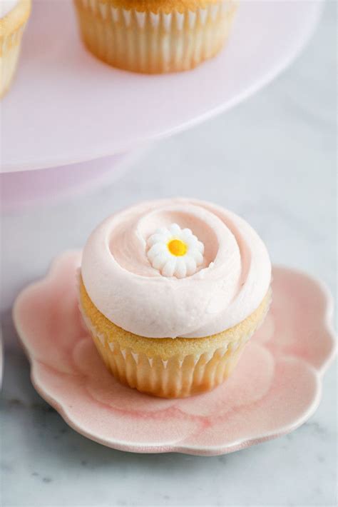 Two Cupcakes With White Frosting And A Flower On Top Are Sitting On