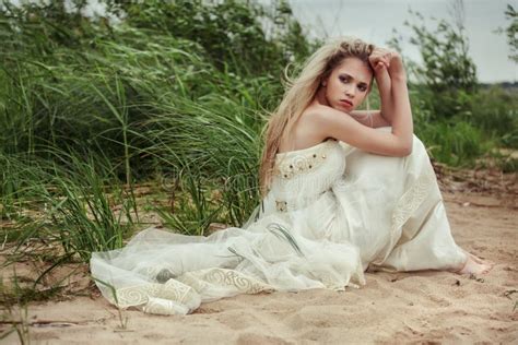 La Belle Fille Dans Une Robe Blanche S Assied Sur La Plage Et Regarde